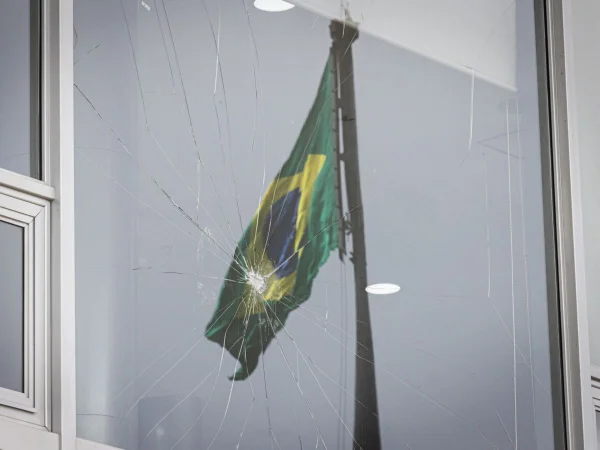 Foto colorida de bandeira brasileira refletida em vidro quebrado - Metrópoles