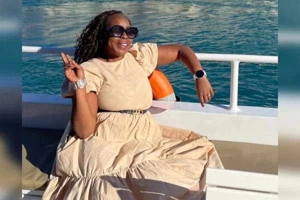 Foto colorida de mulher com vestido longo bege, dentro de um barco, posando para foto em alto mar - Metrópoles.