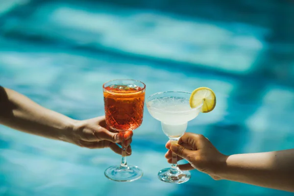 duas pessoas segurando dois drinks na piscina