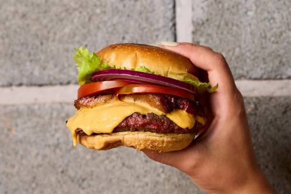 Imagem em close-up de uma mão segurando um hamburguer. Conceito de fast-food, ultraprocessado. Metrópoles