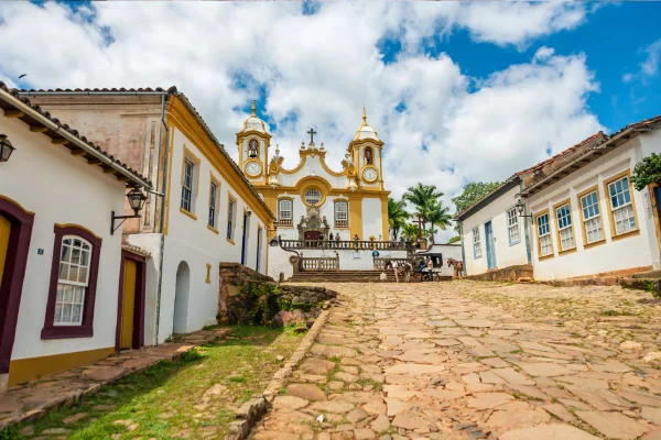 Rua de pedra ladeada por casas coloniais e igreja colonial ao fundo