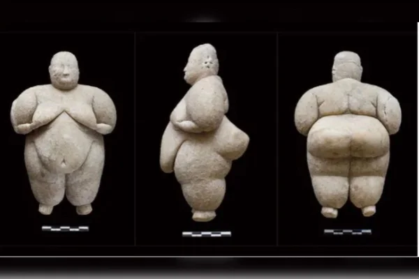 Estátua pequena de pedra, cor cinza, corpo feminino, com fundo preto - Metrópoles
