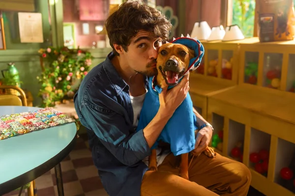 Imagem colorida de Rafa Vitti sorrindo para a foto com o cachorro Amendoim, no set de Caramelo, da Netflix