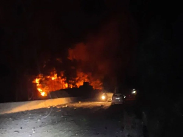 Fotografia noturna mostra incêndio em curso. Há um veículo parado numa estrada e outro, iluminando parte da cena. Foto mostra incêndio após ataque israelense a Masyaf, na província de Hama, região central da Síria