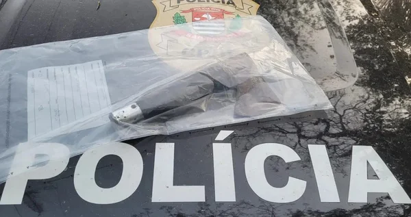 Imagem colorida mostra uma faca com cabo preto embalada em envelope plástico, em cima de capô de carro da Polícia Civil - Metrópoles