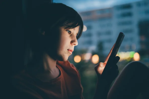 Foto colorida de adolescente mexendo no celular em um querto escuro. Foto ilustrtiva - Metrópoles
