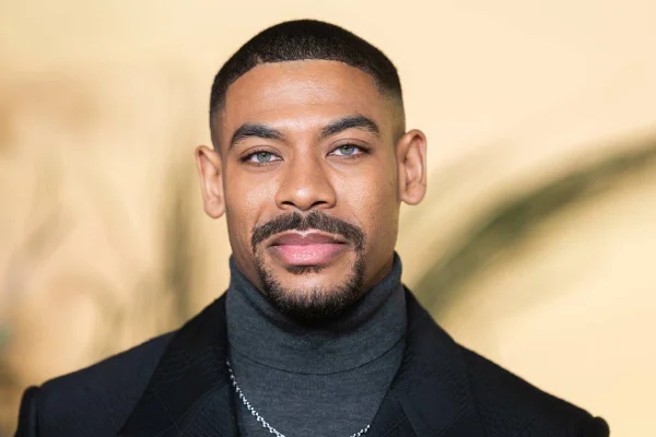 Imagem colorida de homem usando roupa formal preta, com olhos claros e sorriso - Metrópoles