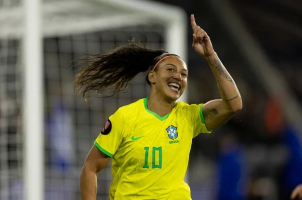 Foto mostra a atacante brasileira Bia Zaneratto com a camiseta amarela da seleção feminina, apontando para cima com um gol ao fundo - Metrópoles
