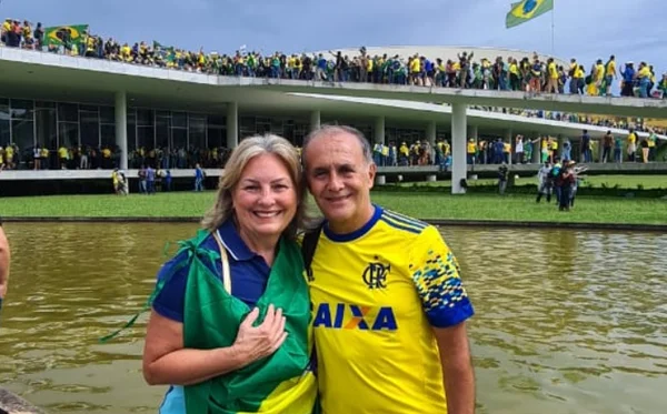 Vilmar José Fortuna. capitão da Marinha, em ato golpista que destruiu prédios públicos na Esplanada dos Ministérios no domingo. Ele posa ao lado de sua esposa, ambos sorrindo, enquanto Congresso Nacional é invadido atrás - Metrópoles