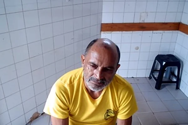 Homem careca sentado com camisa amarela em sala branca