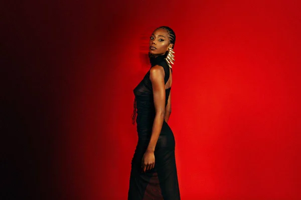 foto colorida de mulher negra de vestido preto em fundo vermelho - metrópoles