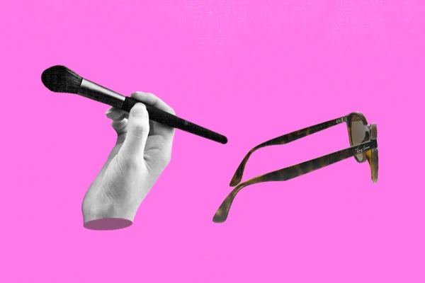 Mão segura pincel de maquiagem em um fundo rosa, matéria sobre falta de acessibilidade no mercado da beleza para deficientes visuais - Metrópoles