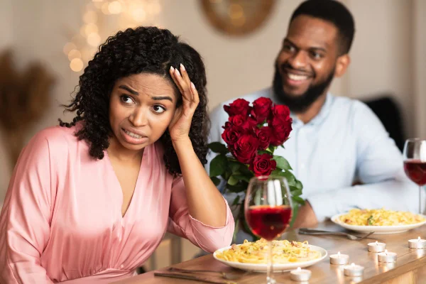 Foto colorida de um casal negro em um jantar romântico a mulher está claramente incomodada com o encontro