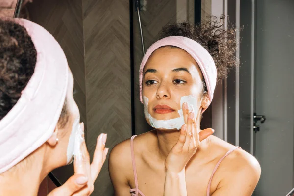 Mulher de frente para o espelho aplicando produto no rosto