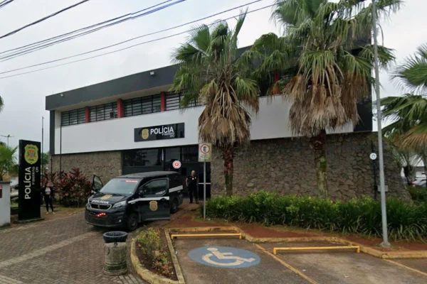 imagem colorida mostra fachada da central de polícia judiciária de praia grande. uma viatura está estacionada em frente à porta de entrada do prédio