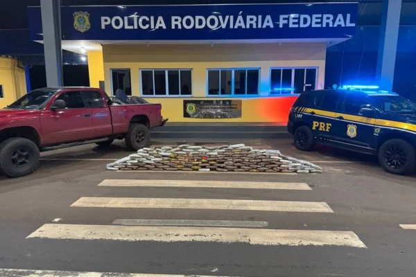 Imagens coloridas mostram tablets de drogas empilhados em frente de uma unidade da PRF e duas viaturas, uma de cada lado