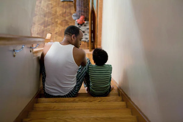 Foto colorida de um adulto ao lado de uma criança sentado no degrau de uma escada, os dois estão conversando - Metrópoles