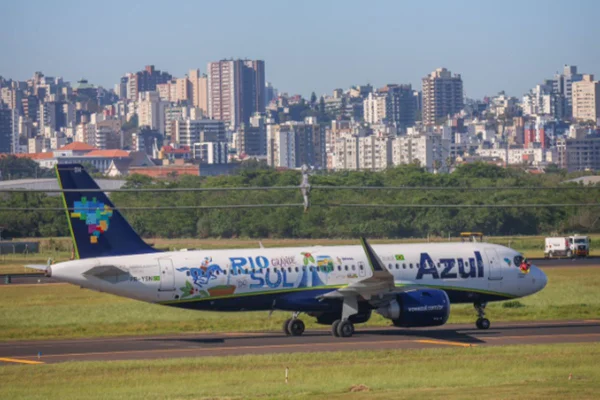 Imagem colorida de aviao em pista de aeroporto com Porto Alegre ao fundo - Metrópoles