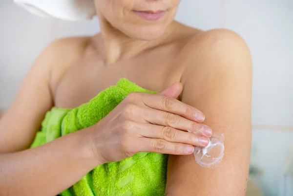 Mulher de toalha aplica gel de testosterona no braço - Metrópoles