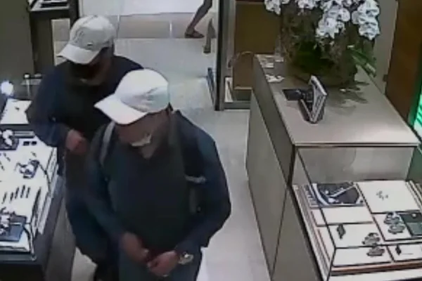 Imagem colorida: dois homens de boné caminham em joalheria - Metrópoles