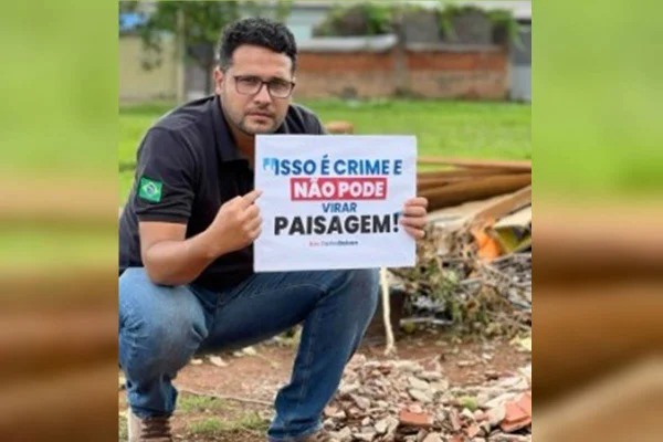 Homem agachado segura placa contra descarte de lixo irregular - Metrópoles