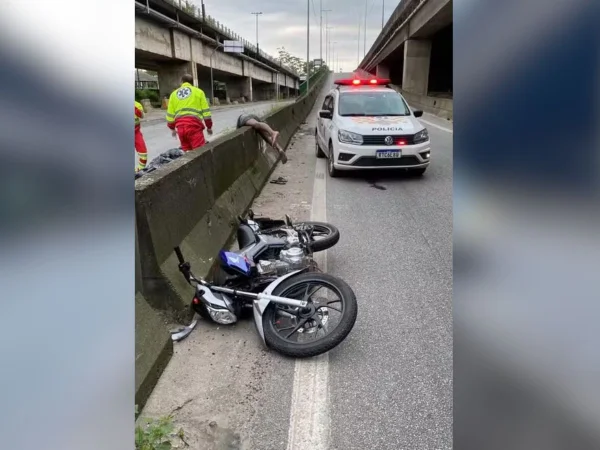 Imagem colorida mostra corpo estendido em cima de uma mureta ao lado de um carro da PM - Metrópoles