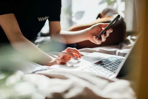 Na foto há uma pessoa segurando um celular e mexendo no computador - Metrópoles
