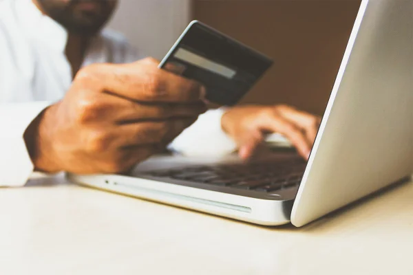 Pessoa digita em computador enquanto segura cartão de crédito - Metrópoles