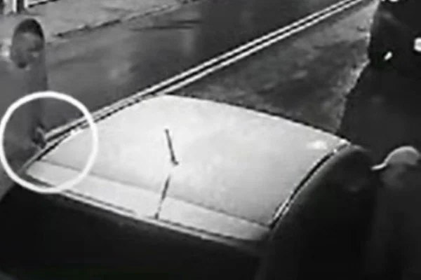 Imagem preto e branca de homens abordando um veículo com uma mulher dentro durante a noite - Metrópoles