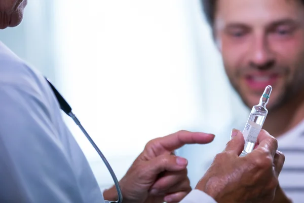 Foto colorida de médico mostrando ampola com testosterona para homem em segundo plano - Metrópoles.