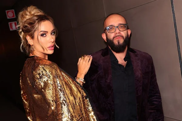 Foto colorida de mulher loira, com mão no ombro de homem, com blazer de veludo na cor vinho - Metrópoles