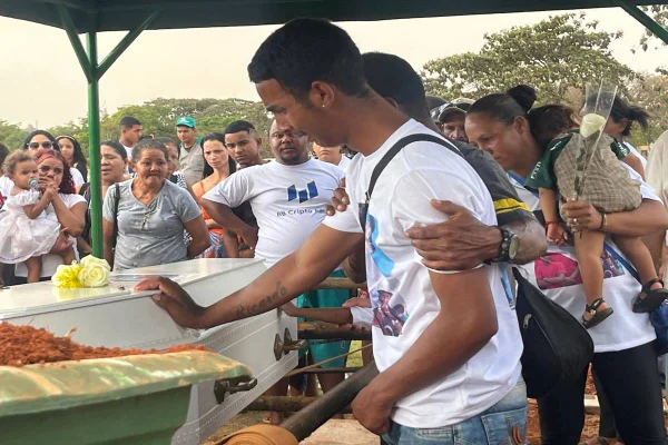 Foto colorida de pessoas sepultando um caixão com criança