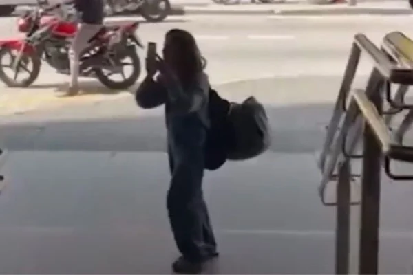 Imagem colorida mostra mulher segurando um celular fazendo uma filmagem na calçada - Metrópoles