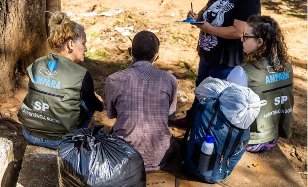 Imagem colorida de assistentes sociais conversando com morador de rua
