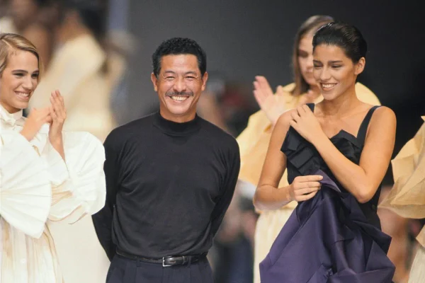 Estilista japonês Issey Miyake, em passarela, sorrindo, ao lado de modelos que o aplaudem