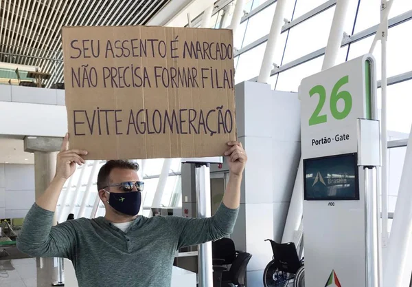 Homem com placa no aeroporto, pedindo fim das filas e aglomeração