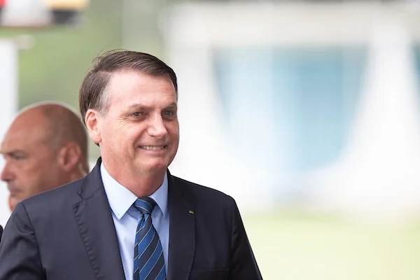 Presidente Bolsonaro sorri do lado de fora do palácio da Alvorada, no cercadinho onde ficam seus apoiadores e jornalistas. Ele usa terno - Metrópoles