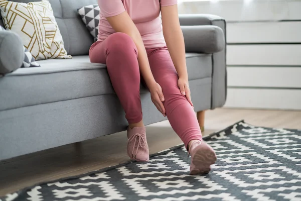 Mulher sentada em sofá com as mãos em perna inchada - Metrópoles