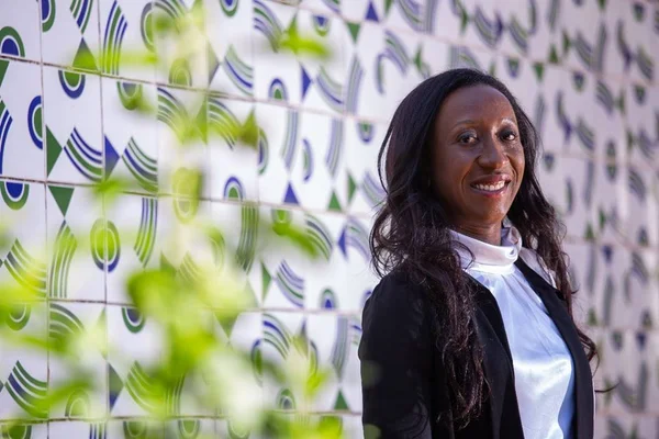 mulher negra sorrindo na frente de parede com mosaico