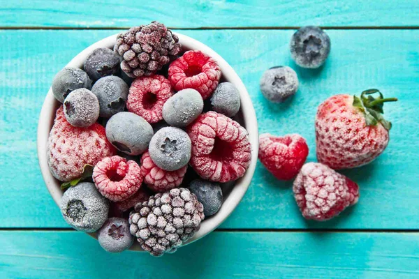 Foto mostra pode de frutas vermelhas congeladas. Nele há mirtilos, morangos e amoras