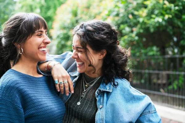 Foto colorida de mulher sorrindo apoiada no ombro da amiga - Psicólogo explica qual é o verdadeiro marcador da felicidade - Metrópoles