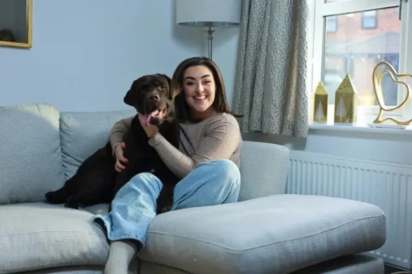 Foto colorida de mulher sentada em sofá abraçando cachorro - Metrópoles