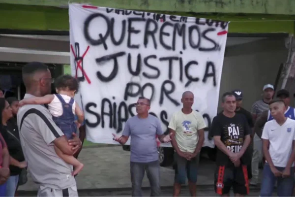 Imagem em cores mostra um protesto realizado por familiares de duas crianças atropeladas. Ao fundo, uma faixa escrito "Queremos Justiça por Isaías e Sophia".