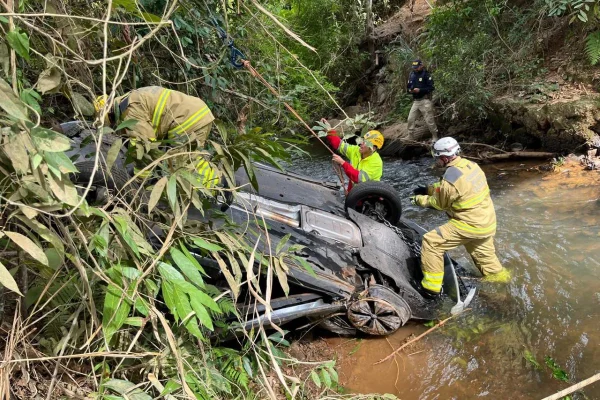 Imagem colorida mostra bombeiros retirando carro de ribanceira após bater em muro de concreto e sair da pista - Metrópoles