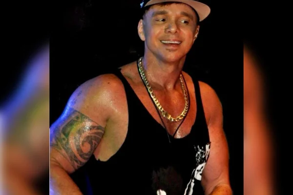 Foto colorida de homem com blusa preta e boné, olhando para o lado e sorrindo para foto - Metrópoles.