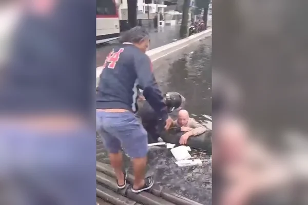 Imagem colorida de um idoso sendo resgatado de um canal por populares durante um temporal - Metrópoles