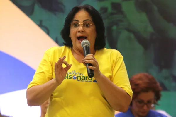 Damares Alves vestida com camiseta amarela e falando ao microfone