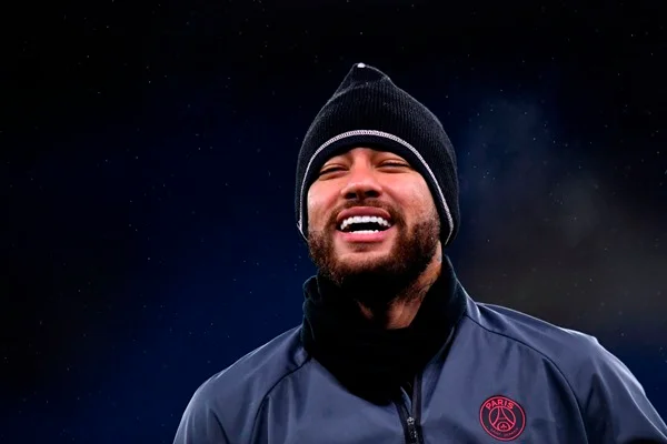 Neymar Júnior, jogador brasileiro de futebol. Ele tem cabelos escuros, usa uniforme de time de futebol e sorri enquanto olha para a frente - Metrópoles