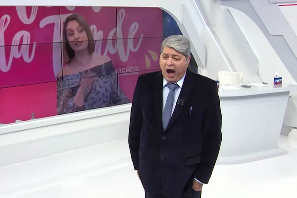 Datena boceja ao vivo no programa Brasil Urgente e diz que está com um "sono desgraçado". No painel ao fundo, a apresentadora Catia Fonseca, ambos da Band -Metrópoles