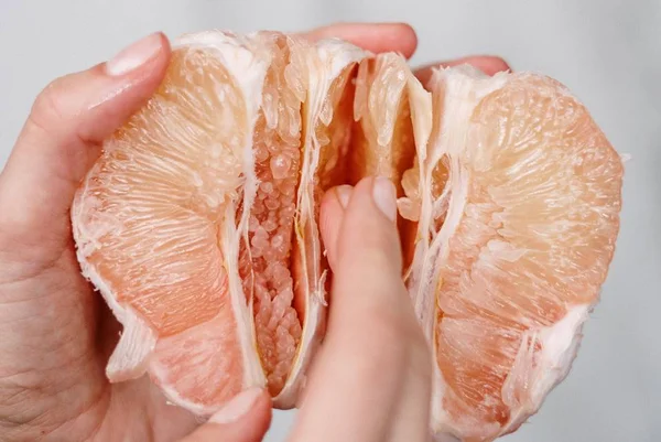 Foto colorida de duas mãos segurando uma toranja e passando os delos no meio da fruta, em close - Metrópoles